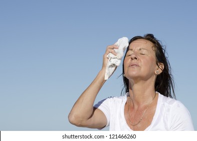 Portrait of stressed and exhausted looking middle aged woman trying to cool down face, isolated outdoor with blue sky as background and copy space. - Powered by Shutterstock