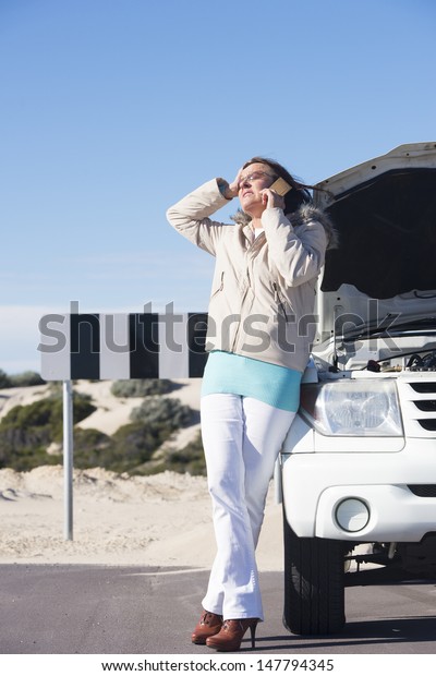 Portrait stressed mature woman breakdown\
with car calling for service, assistance for help on mobile phone,\
with blue sky as background and copy\
space.