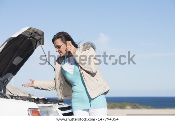 Portrait stressed mature woman breakdown\
with car calling for service, assistance for help on mobile phone,\
with blue sky as background and copy\
space.