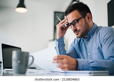 Portrait of stressed out and worried troublesome overworked businessman entrepreneur looking documents report in modern bright office working under pressure and tight deadline