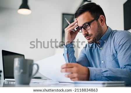 Portrait of stressed out and worried troublesome overworked businessman entrepreneur looking documents report in modern bright office working under pressure and tight deadline