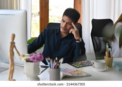 A portrait of a stressful Asian designer or a creative worker sitting in the office and working on designing on a computer, for art, design, and business concept. - Powered by Shutterstock