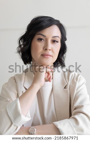 Portrait of a strict middle-aged brunette woman in a beige jacket. He looks at the camera, resting his chin on his hand. Business portrait.