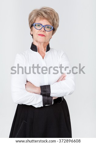 Portrait of strict senior Caucasian woman with folded arms, gray background