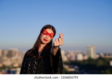 Portrait of strong brunette superwoman in black dress and red face mask showing korean heart at urban city background. Female power, women rights, activism concept. Protesting for freedom and equality - Powered by Shutterstock