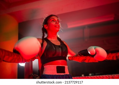 Portrait Of Strong Female Boxer Relaxing After Match. Low Angle View Of Pretty Girl Calmly Leaning On Ropes Of Ring In Corner Gathering Her Strength After Bout. Female Boxing, Active Lifestyle Concept