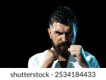 Portrait of strong karate man in kimono at gym. Bearded male practicing aikido. Handsome muscular fighter ready for karate training. Serious karate man in fighting position preparing for competition.