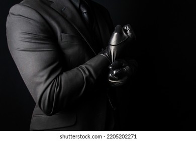 Portrait Of Strong Man In Dark Suit Pulling On Black Leather Gloves. Concept Of Mafia Hitman Or Gentleman Assassin