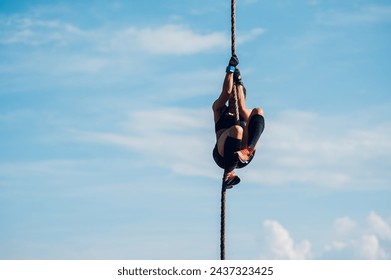 Portrait of a strong woman athlete partake in one of the events of an obstacle course race. Female working out outside and climbing the rope during a race. Sport competition and OCR race. Copy space. - Powered by Shutterstock