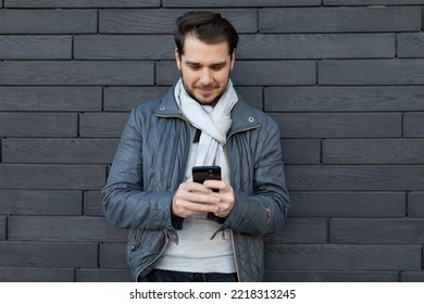 Portrait Of A Strong Young Man With A Phone In His Hands Against A Gray Wall, Entrepreneurship Development And Business Planning Concept