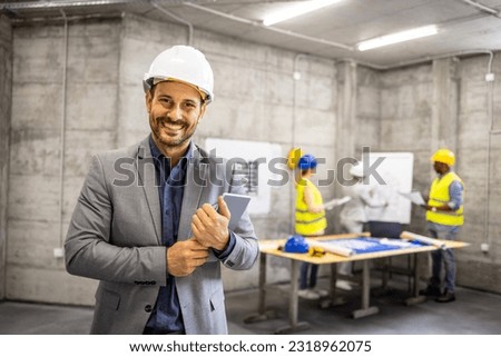 Portrait of structural engineer in business suit and hardhat holding tablet computer at construction site.