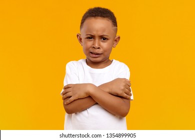 Portrait Of Stubborn Reluctant Black Dark Skinny Child Posing In Studio With Grumpy Dissatisfied Grimace, Keeping Arms On His Chest, Demonstrating Unwillingness To Clean His Room. Body Language