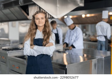 Portrait of student girl chef wearing apron standing with crossed arms study cooking class in kitchen at school - Powered by Shutterstock