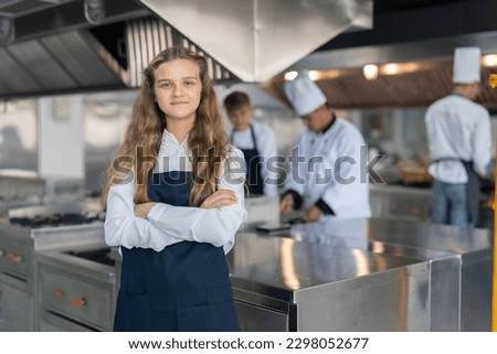 Portrait of student girl chef wearing apron standing with crossed arms study cooking class in kitchen at school