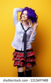 Portrait of a student girl with purple hair in white blouse and checkered skirt posing on yellow background at studio. Japanese style anime. 