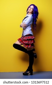 Portrait of a student girl with purple hair in white blouse and checkered skirt posing on yellow background at studio. Japanese style anime. 