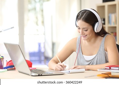 Portrait of a student learning on line with headphones and laptop taking notes in a notebook sitting at her desk at home