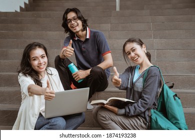 Portrait students sit down working in groups on the floor stairs campus looking at camera showing thumbs