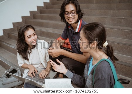 Portrait students sit down working in groups on the floor stairs campus