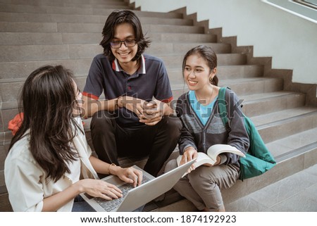 Portrait students sit down working in groups on the floor stairs campus