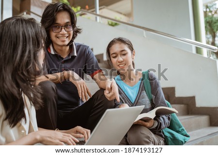 Portrait students sit down working in groups on the floor stairs campus