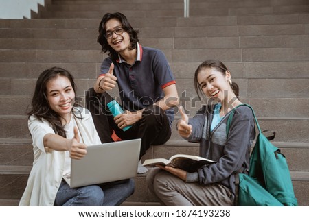 Portrait students sit down working in groups on the floor stairs campus looking at camera showing thumbs
