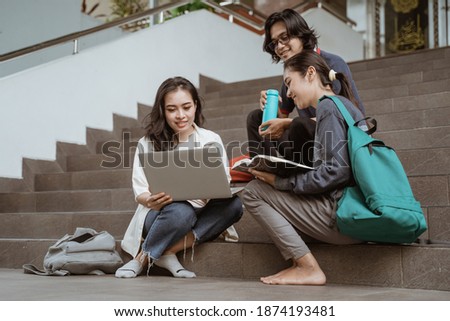 Portrait students sit down working in groups on the floor stairs campus