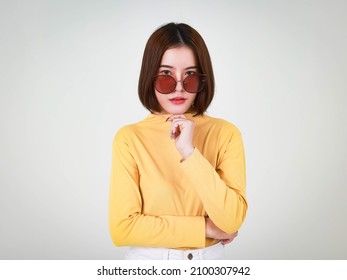 Portrait Studio Cutout Shot Of Asian Young Beautiful Stylish Short Hair Female Model In Yellow Long Sleeve Shirt Standing Crossed Arm Holding Hand Adjusting Fashion Sunglasses On White Background.