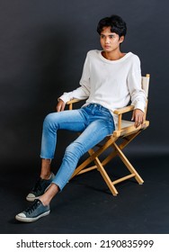 Portrait Studio Full Body Shot Of Asian Young LGBTQ Gay Glamour Handsome Bisexual Homosexual Male Model In Casual Outfit Sitting Crossed Legs On Wooden Chair Posing Gesturing On Black Background.