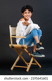 Portrait Studio Full Body Shot Of Asian Young LGBTQ Gay Glamour Handsome Bisexual Homosexual Male Model In Casual Outfit Sitting Crossed Legs On Wooden Chair Posing Gesturing On Black Background.