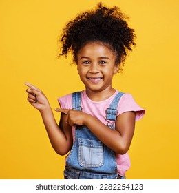 Portrait  studio   happy child pointing hand at space and smile face yellow background  Young girl kid and happiness  carefree   positive attitude to show product placement mockup deal