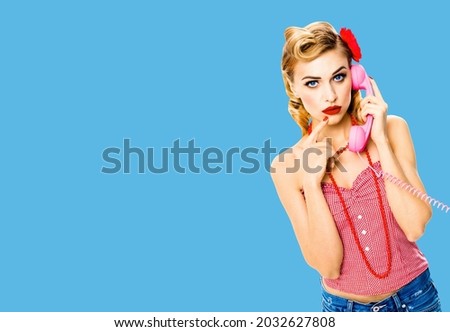 Portrait studio image - pensive, puzzled or thinking woman with phone tube. Unhappy pin up girl. Retro and vintage concept. Bright blue color background with copy space area. Call centre. Callcentre.