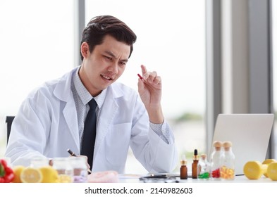 Portrait Studio Shot Asian Male Professional Nutritionist Dietitian Doctor In White Lab Coat And Stethoscope Sitting Holding Pen Smiling At Working Desk Full Of Fruits Vegetable Nutrition Supplements.