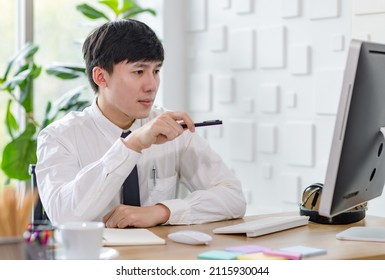 Portrait Studio Shot Of Asian Professional Successful Male Businessman Employee In Formal Shirt With Necktie Sitting Look At Camera At Working Desk With Computer Monitor Keyboard Mouse And Stationery.