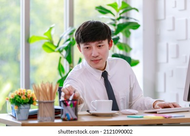 Portrait Studio Shot Of Asian Professional Successful Male Businessman Employee In Formal Shirt With Necktie Sitting Look At Camera At Working Desk With Computer Monitor Keyboard Mouse And Stationery.