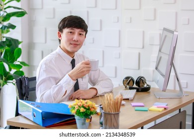 Portrait Studio Shot Of Asian Professional Successful Male Businessman Employee In Formal Shirt With Necktie Sitting Look At Camera At Working Desk With Computer Monitor Keyboard Mouse And Stationery.