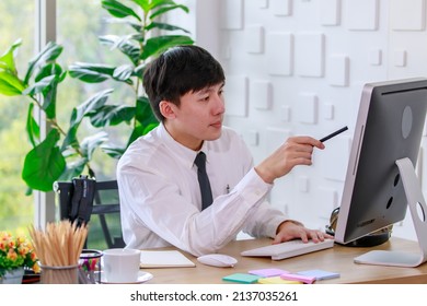 Portrait Studio Shot Of Asian Professional Successful Male Businessman Employee In Formal Shirt With Necktie Sitting Look At Camera At Working Desk With Computer Monitor Keyboard Mouse And Stationery.