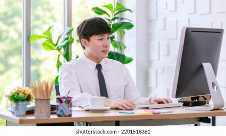 Portrait Studio Shot Of Asian Professional Successful Male Businessman Employee In Formal Shirt With Necktie Sitting Look At Camera At Working Desk With Computer Monitor Keyboard Mouse And Stationery.