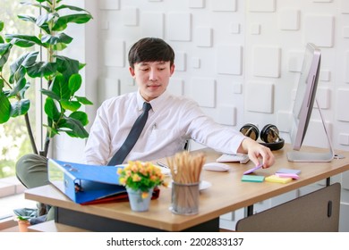 Portrait Studio Shot Of Asian Professional Successful Male Businessman Employee In Formal Shirt With Necktie Sitting Look At Camera At Working Desk With Computer Monitor Keyboard Mouse And Stationery.