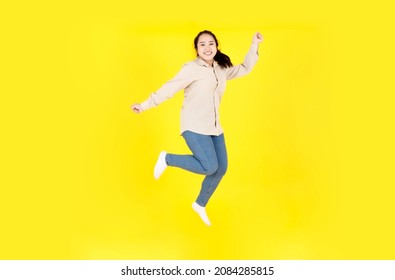 Portrait studio shot of Asian young happy female chubby plump model in casual outfit long sleeve shirt and denim jeans pants smiling look at camera jumping high exercise alone on yellow background.