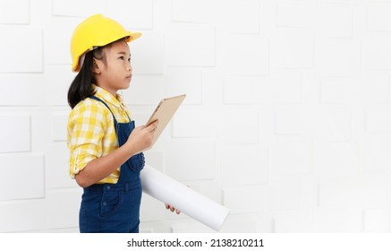 Portrait studio shot Asian young little elementary schoolgirl future dream job career as engineer and architect wears yellow safety hardhat helmet standing look at camera holding tablet and blueprint.