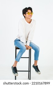 Portrait Studio Shot Of Asian Young LGBT Gay Happy Bisexual Homosexual Male Fashionable Model In Casual Outfit Fashion Sunglasses Standing Leaning At Tall Chair Smiling Posing On White Background.