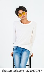 Portrait Studio Shot Of Asian Young LGBT Gay Happy Bisexual Homosexual Male Fashionable Model In Casual Outfit Fashion Sunglasses Standing Leaning At Tall Chair Smiling Posing On White Background.