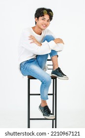 Portrait Studio Shot Of Asian Young LGBT Gay Happy Bisexual Homosexual Male Fashionable Model In Casual Outfit Fashion Sunglasses Standing Leaning At Tall Chair Smiling Posing On White Background.