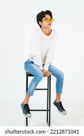 Portrait Studio Shot Of Asian Young LGBT Gay Happy Bisexual Homosexual Male Fashionable Model In Casual Outfit Fashion Sunglasses Standing Leaning At Tall Chair Smiling Posing On White Background.