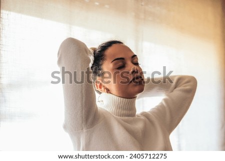 Portrait of a stunning young woman putting up her hair near a window. 