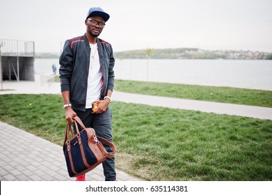 Portrait Of Stylish African American Man On Sportswear, Cap And Glasses Walking With Handbag. Black Men Model Street Fashion.