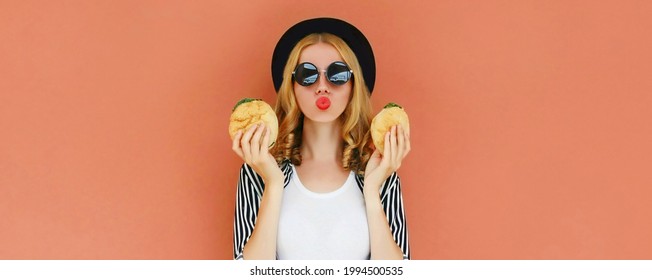 Portrait Of Stylish Attractive Young Woman Blowing Her Lips And Showing A Two Burger Fast Food On Brown Background