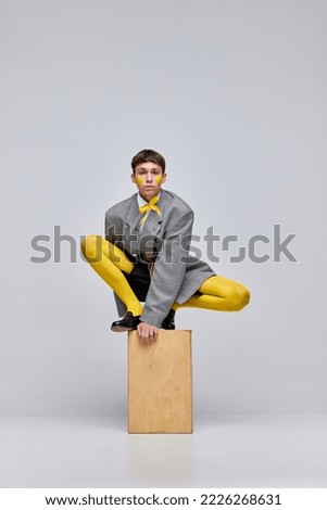 Portrait of stylish boy posing in jacket, blazer and yellow tights isolated over grey background. Weird teen, glamour . Concept of modern fashion, art photography, style, queer, uniqueness, ad