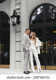 Portrait Of Stylish Brides Couple Man And Woman In White Wedding Suit Looking At Each Other. Posing Near Modern Building Restaurant. Modern Wedding. Happy Married Couple. Marriage.